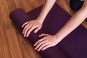 Young yoga girl rolling her violet mat after doing yoga on a woo