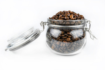 Fresh, roasted coffee beans in a open transparent jar standing on a white table.