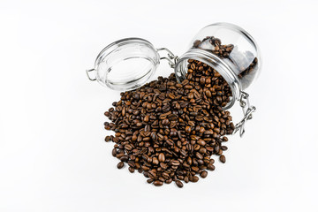 Fresh, roasted coffee beans in a open, overturned jar on a white table.