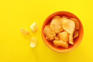 Top view image of potato chips slices in the bowl over yellow background