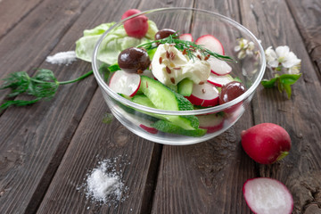Side view of radish and cucumber salad with sour cream in a glass bowl on wooden background