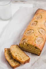 Homemade sliced healthy banana bread ready for serve on breakfast on the white concrete background with craft baking paper and pastry knife, glass of milk. Top view. Close up shoot