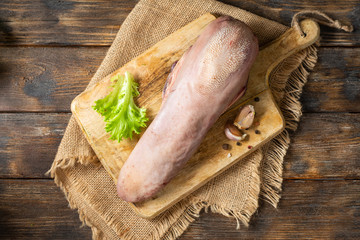 Beef tongue on a wooden Board on a brown wooden table. Raw beef tongue on the kitchen table. Top view with space for text