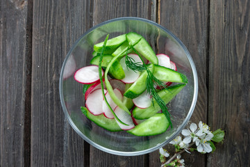 Top view of fresh radish and cucumber salad on wooden background