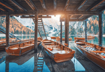 Wooden boats under the house in famous Braies lake at sunrise in autumn in Dolomites, Italy. Landscape with stairs, mountains, blue water, colorful trees in fall in dawn. Travel in Europe. Alps