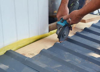 A building contractor is cutting lightweight metal, steel, corrugated, paint coated roofing sheet...