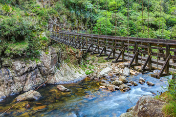 A wooden suspension bridge in a rocky river valley. Karangahake Gorge, New Zealand