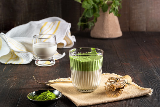 Matcha green tea latte with matcha powder and bamboo whisk on wood background.