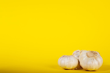 3 heads of garlic on a yellow background.