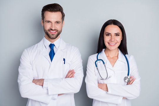 Photo of handsome doc guy professional lady patient consultation virology clinic listen client toothy smiling arms crossed experienced doctors wear lab coats isolated grey color background