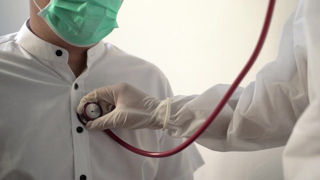 Coronavirus concept. Close up Asian male doctor hands in a rubber medical glove listens to the breath of an elderly sick man using a phonendoscope. 4K Resolution.