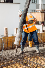 Mason building and worker using a automatic cement pump and leveling a first layer of fresh concrete floor at house, construction site
