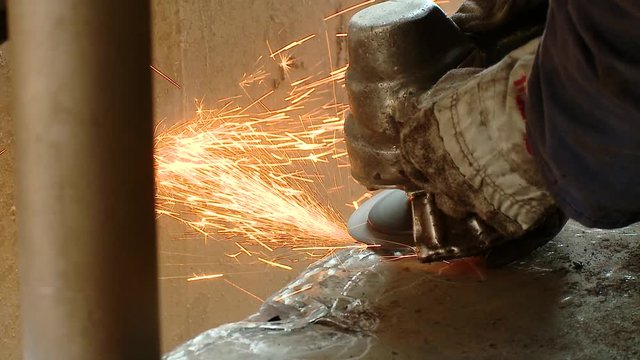 A close-up of a metal worker grinding an edge of a steel plate with sparks