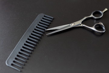 hairdresser tool scissors and comb on a black background, place for an inscription