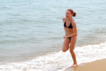   girl in a swimsuit runs along the sandy beach along the sea
