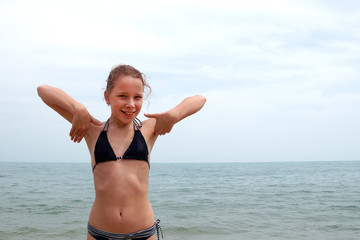 girl in a swimsuit at sea rejoices with hands up
