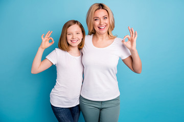 Photo of two people young beautiful mom lady small daughter good mood showing okey symbols express agreement wear casual white s-shirts isolated blue color background