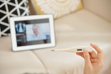 Hand of young woman measuring her temperature when consulting with doctor via application on tablet computer