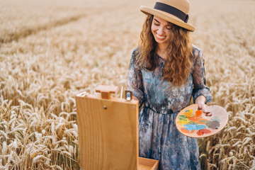 Portrait of smiling female artist with curly hair in hat. Girl draws a picture of a landscape in a...