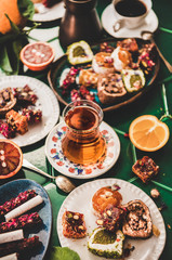 Variety of Turkish traditional lokum sweet delight with Turkish coffee in cups, tea in tulip glass and fresh fruits over green Moroccan tile table, top view. Middle East typical dessert food