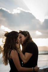 Pareja de dos chicas morenas jóvenes que son novias lesbianas besándose en la playa junto al mar