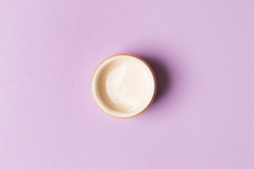 opened jar with cream on purple background. top view