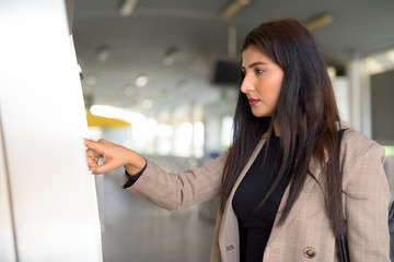 Profile view of young beautiful Indian businesswoman buying ticket at skytrain station