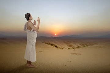 Asian Muslim man in ihram clothes standing and praying while raised arms