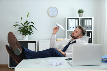 Lazy young man playing with paper plane in office
