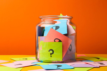 Colorful cards with question marks in glass jar on orange background