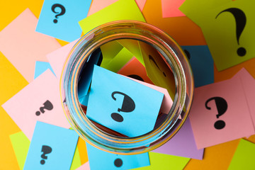 Colorful cards with question marks and glass jar on yellow background, top view