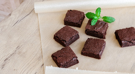 Freshly baked classic fudge brownie on parchment brown paper and wooden table background. Homemade sweet food. 