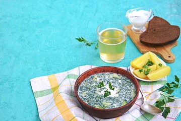 Okroshka, traditional Russian cold soup on kvass with fresh cucumbers, boiled potatoes and meat in a clay bowl on a turquoise background. Served with boiled potatoes and rye bread. Russian cuisine.