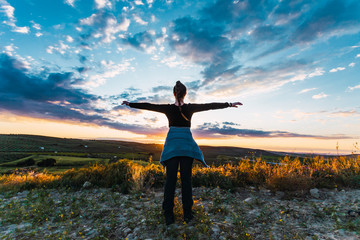 Young woman looks at the sun and the sky with open arms.