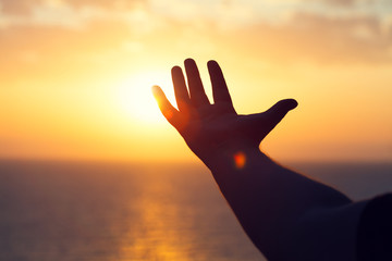 young man raising hands praying at sunset or sunrise light, dreams, freedom and spirituality concept