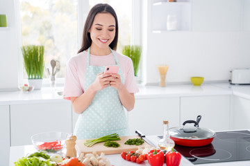 Portrait of her she nice attractive lovely cheerful cheery girl preparing cooking everyday domestic lunch veg using device searching creative blog influencer in modern light white interior kitchen