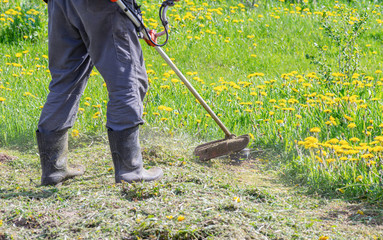 Closeup of a worker in special clothes with a gas mower in his hand.