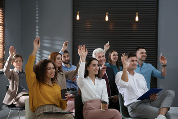 People raising hands to ask questions at seminar in office