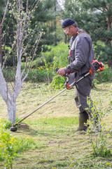 Farmer mows grass in the spring garden. The concept of care for a personal plot.