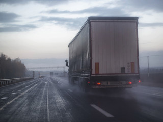 Obraz na płótnie Canvas A truck wagon rides on a highway with poor visibility where it rains and fog, background. Bad Road Safety Concept, copy space