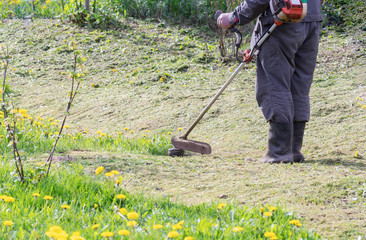 Closeup of a worker in special clothes with a gas mower in his hand.