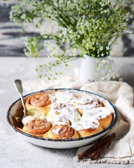 Cinnamon buns in a baking dish with cream cheese curd on a gray background
