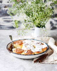 Cinnamon buns in a baking dish with cream cheese curd on a gray background