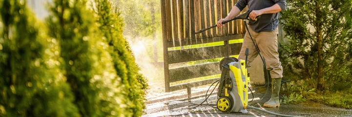 Unrecognizable man cleaning a wooden gate with a power washer. High pressure water cleaner used to...