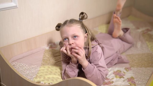 Sad 8 year old in a children's room on a children's sofa lies and thinks dangles legs, sharp picture