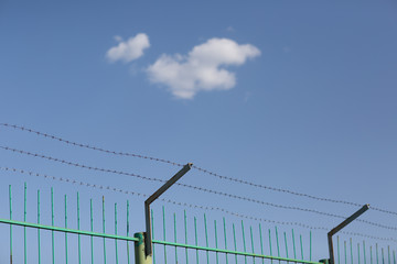 Lonely cloud in blue sky behind barbed wire