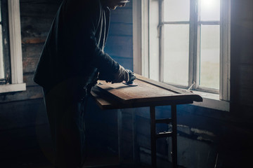 Fototapeta premium elderly man polishes a wooden board with a grinder at home. Furniture restoration, housework.