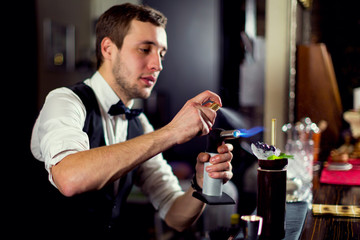 A young guy working as a bartender behind a bar is preparing drinks for customers.
