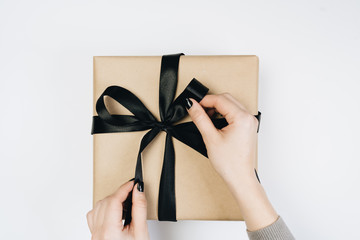 Partial view of woman tying ribbon on gift box isolated on white
