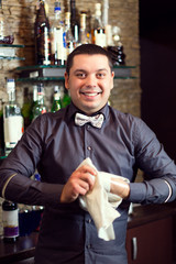 A young guy working as a bartender behind a bar is preparing drinks for customers.
